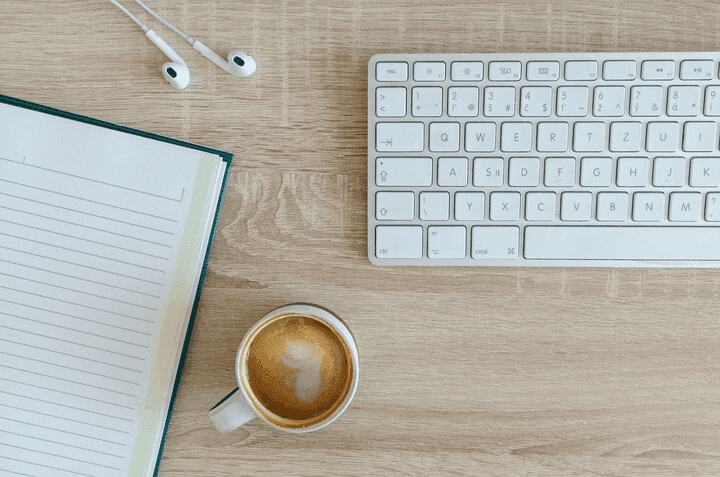 An overhead view of a desk with an open notebook, keyboard, earphones and a cup of coffee.